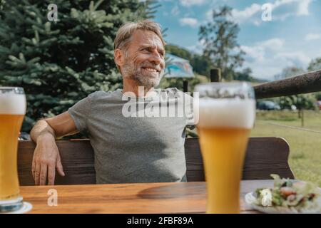 Lächelnder reifer Mann schaut weg, während er im Biergarten sitzt Stockfoto