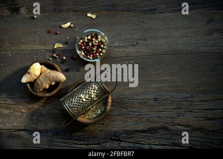 Schüsseln mit Ingwerwurzel, alter Reibe und verschiedenen Pfefferkörnern liegen auf Holzoberfläche Stockfoto