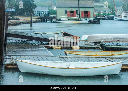 Boote am Dock im Regen mit dem Yachthafen festgebunden Gebäude und Segelboote im Hintergrund und ein paar zu Fuß Über eine Eingangsrampe Stockfoto