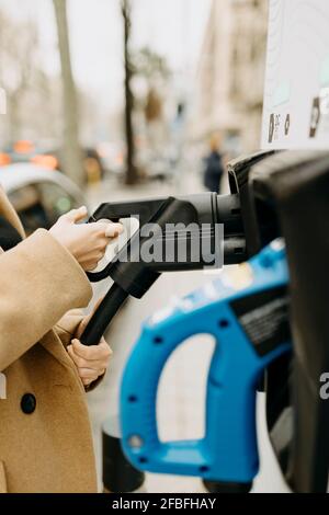 Frau, die Kabel eines Elektroautos an der Ladestation hält Stockfoto