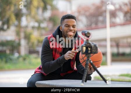 Hübscher junger Influencer vloggt, während er auf Basketball zeigt Stockfoto