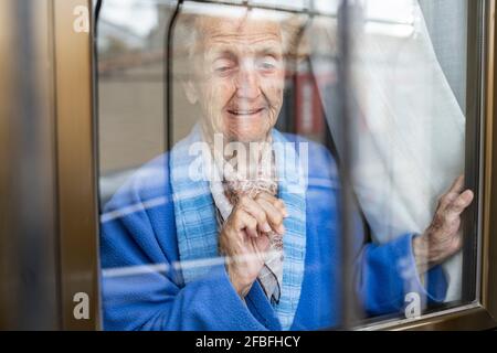 Ältere Frau schaut durch das Fenster des Hauses Stockfoto