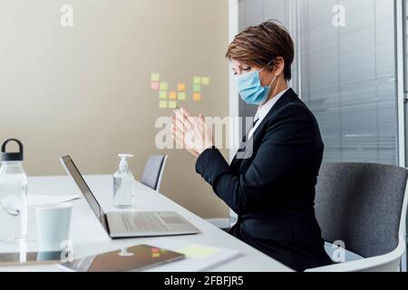 Weibliche Profi mit Schutzmaske reiben Hände während der Verwendung Desinfektionsmittel am Schreibtisch im Büro Stockfoto