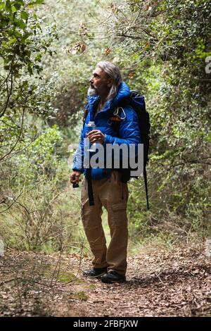 Männlicher Entdecker, der Wasserflasche hält, während er Pflanzen ansieht Wald am Wochenende Stockfoto
