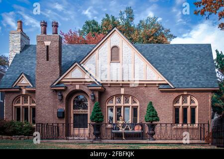 Charmantes Backstein Vintage Cottage mit Herbstfarben und einem Halloween Skelett auf der Bank vor der Haustür - gewölbte Fenster Und Tür Stockfoto