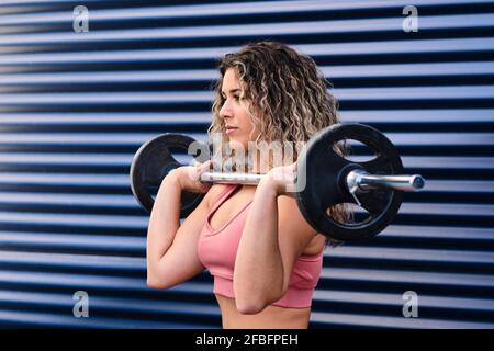 Junge Sportlerin trainiert mit Barbel an blauer Wand Stockfoto