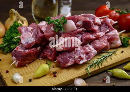 Rohe Schweinespieße bereit für Grill mit verschiedenen frischen Gemüse auf einem Holztisch. Selektiver Fokus. Stockfoto