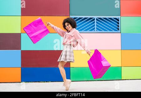 Fröhliche Frau mit Einkaufstaschen, die auf Zehenspitzen von Colorful stehen Wand Stockfoto