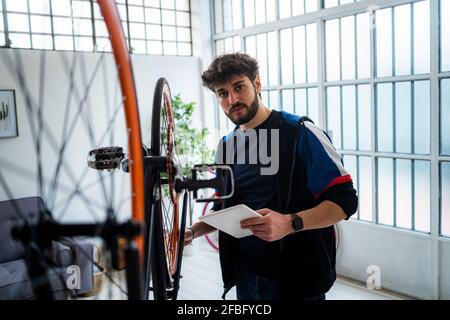 Junger Mann mit digitalem Tablet, der zu Hause Fahrrad repariert Stockfoto