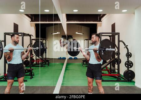 Sportler, der im Fitnessstudio neben einem Spiegel steht, die Langhantel hebt Stockfoto