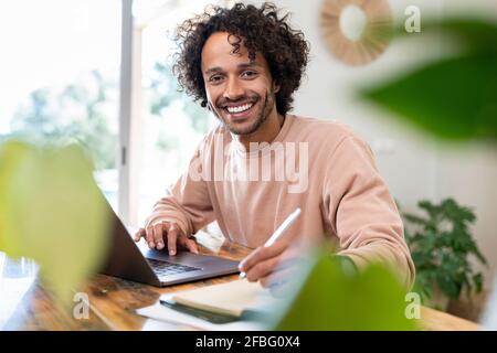 Männlicher Unternehmer mit Laptop, der im Tagebuch auf den Tisch schreibt Zu Hause Stockfoto