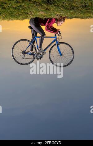 Auf dem Kopf stehendes Bild einer Frau mit Fahrrad, das auf Gras liegt Stockfoto