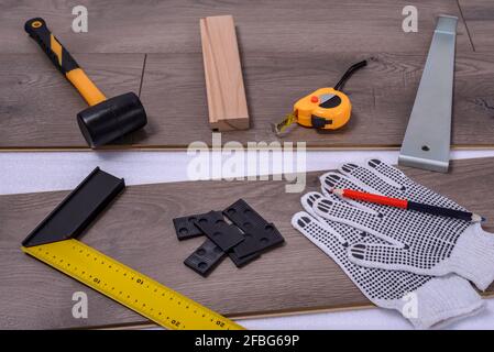 Ausrüstung oder Werkzeuge zum Einbau von Laminatboden. Hammer, Brechstange, Abstandshalter, Hammer, Schutzhandschuhe und Klebeband messen auf dem Laminatboden. Selektive Stockfoto