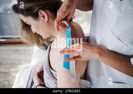 Weibliche Therapeutin klebt elastisches therapeutisches Klebeband an der Schulter des Patienten ein Krankenhaus Stockfoto