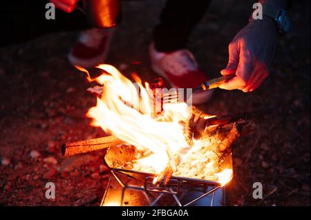 Mann, der Fleisch über dem Holzofen röstet, während er bei zelte Nacht Stockfoto