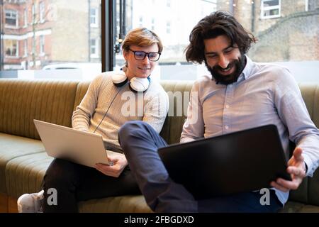 Geschäftsleute mit Laptop diskutieren, während sie auf dem Sofa im Büro sitzen Stockfoto