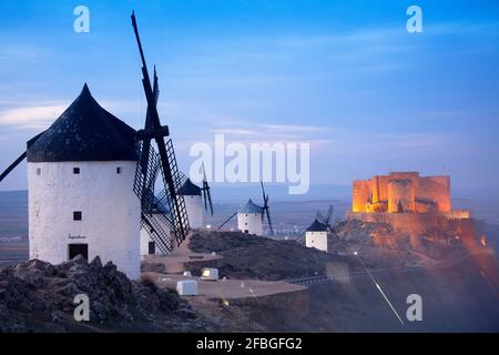 Spanien, Provinz Toledo, Consuegra, Historische Windmühlen in der Abenddämmerung mit Schloss La Muela im Hintergrund Stockfoto