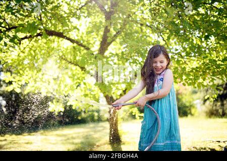 Lächelndes Mädchen, das im Garten durch einen Schlauch wässert Stockfoto