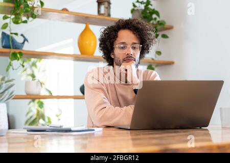 Junger Geschäftsmann mit Brille, während er einen Laptop auf dem Tisch benutzte Zu Hause Stockfoto