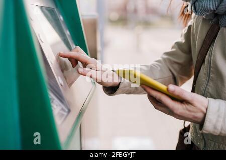 Frau, die den Kiosk in der Hand hält, während sie das Mobiltelefon hält Stockfoto