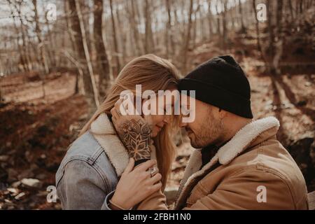 Hipster-Mann, der im Herbst neben der Freundin auf einem Holzgeländer am Wald sitzt Stockfoto