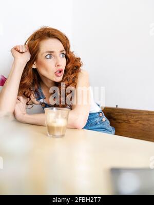 Schockiert, rothaarige Frau weg schauen während der Sitzung mit Getränk am Tisch Stockfoto