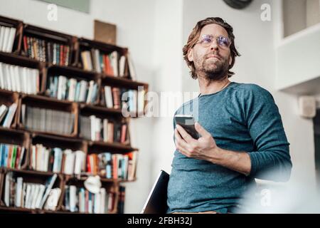 Männlicher Besitzer mit Smartphone, der im Café nachdenkt Stockfoto