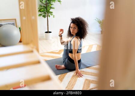 Frau mit lockigen Haaren tut Wirbelsäulendrehung Pose zu Hause Stockfoto