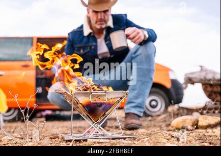 Reifer Mann, der beim Zelten in der Nähe des Holzofens hocken kann Masse Stockfoto