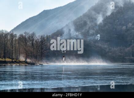 Feuer des Mondonico-Gebirges über dem Ghirla-See mit einem Hubschrauber, der Wasser zum Löschen einlädt, Valganna, Lombardei, Italien. Stockfoto