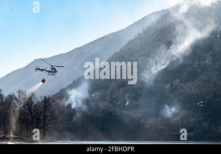 Feuer des Mondonico-Gebirges über dem Ghirla-See mit einem Hubschrauber, der Wasser zum Löschen einlädt, Valganna, Lombardei, Italien. Stockfoto