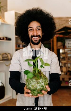 Fröhlicher Mann, der zu Hause Kokedama-Pflanze hält Stockfoto