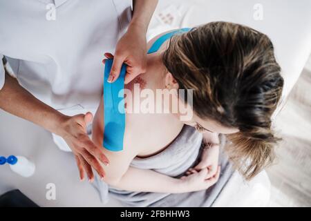 Physiotherapeutin klebt elastisches therapeutisches Klebeband an der Schulter des Patienten In der Klinik Stockfoto