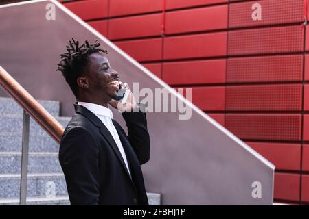 Fröhlicher Geschäftsmann, der Schritt für Schritt auf dem Mobiltelefon spricht Stockfoto
