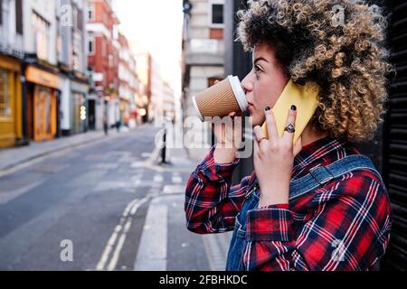 Junge Frau, die Kaffee trinkt, während sie mit dem Handy spricht Stockfoto
