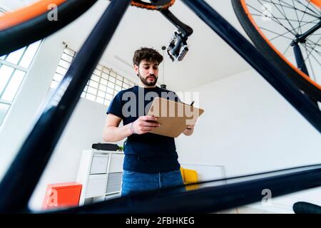 Junger Mann, der Notizen schrieb, während er am Fahrrad stand Zu Hause Stockfoto