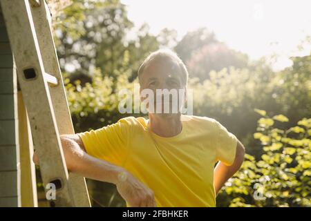 Lächelnder Mann, der sich an sonnigen Tagen auf eine Leiter lehnte Stockfoto