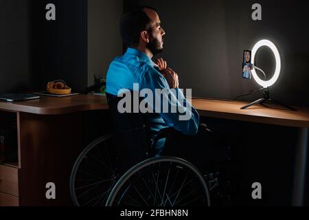 Deaktiviert vlogger binden Krawatte während vlogging durch Mobiltelefon sitzen Im Rollstuhl im Studio Stockfoto