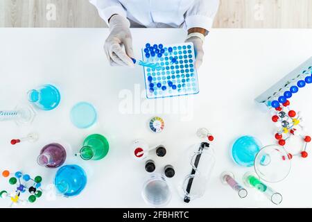 Forscherin, die das Reagenzglas von der Mikrotiterplatte auf dem Tisch entfernt Labor Stockfoto