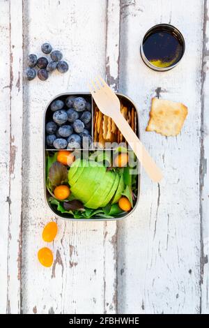 Lunchbox mit Salat, Avocado und gelben Tomaten, Crackern, Blaubeeren und Salatdressing Stockfoto