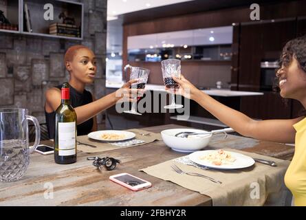 Zwei Freunde, die zu Hause zusammen zu Abend essen und mit Rot rösten Wein Stockfoto