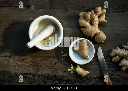 Mörtel und Stößel, Küchenmesser und Ingwerwurzeln liegen auf Holzoberfläche Stockfoto