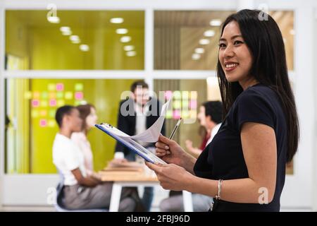 Junge Unternehmerin mit lächelndem Dokument im Büro Stockfoto