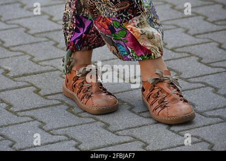 Die Beine der Frau tragen farbenfrohe Hosen und Schuhe mit Schnürsenkeln Ein Straßenpflaster Stockfoto