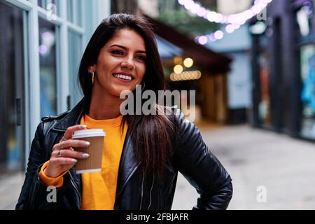 Fröhliche Frau in Lederjacke schaut weg, während sie aufsteht Straße Stockfoto