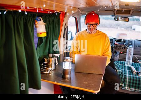 Lächelnder reifer Mann mit Laptop im Wohnheim Stockfoto