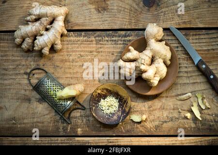 Küchenmesser, Ingwerwurzeln und alte Reibe liegen auf Holzoberfläche Stockfoto