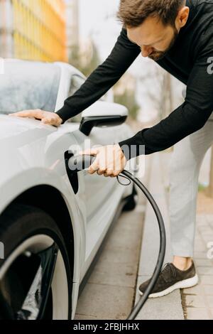 Mann, der an der Ladestation ein Netzkabel in das Auto einsteckt Stockfoto