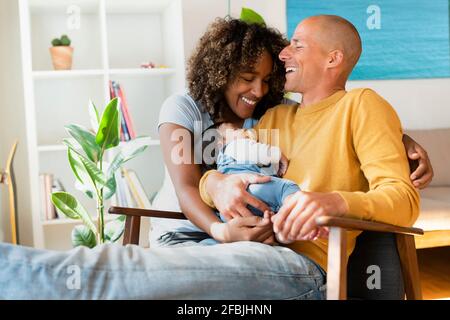 Glückliche Eltern mit schlafenden Babys lachen, während sie zu Hause sitzen Stockfoto