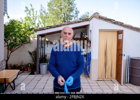 Älterer Mann mit Handschuhen, während er im Hinterhof steht Stockfoto